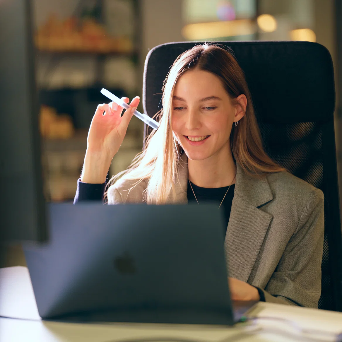 Woman smiling while working on a laptop in an office setting.