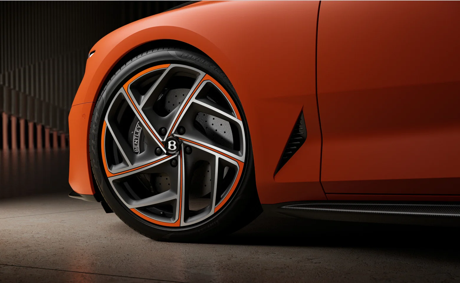 Close-up of Bentley wheel with orange accents and logo.