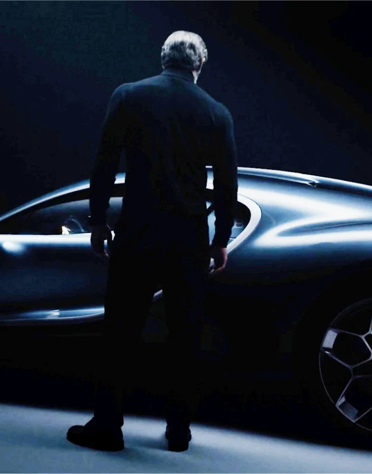Man standing next to a sleek sports car in a dark studio.
