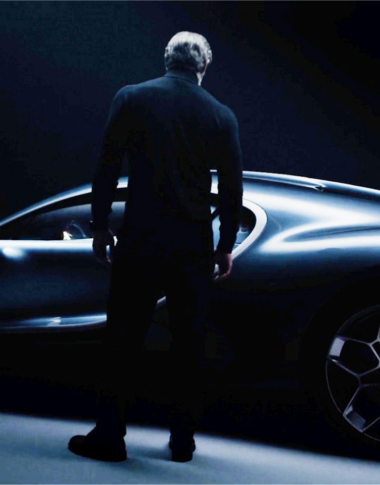 Man standing next to a sleek sports car in a dark studio.
