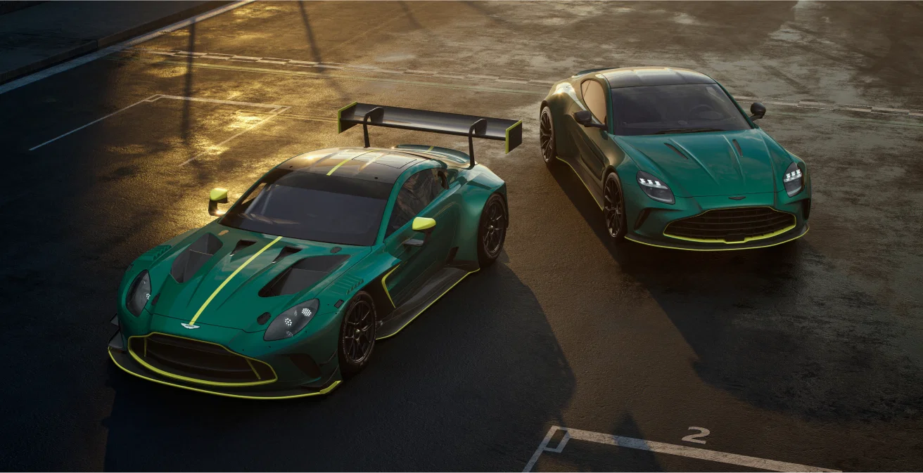 Two green Aston Martin sports cars parked on a racetrack at sunset.